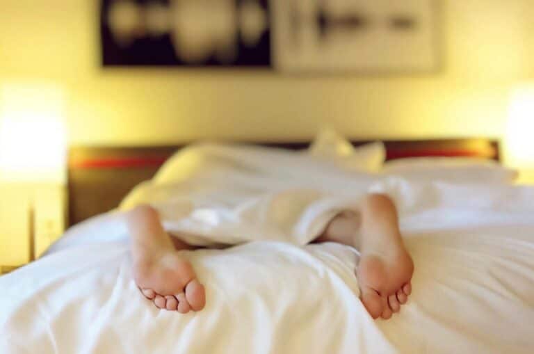 Füße, die unter einer Decke am Ende eines Bettes hervorschauen, symbolisieren die Distanz und den fehlenden sexuellen Ko